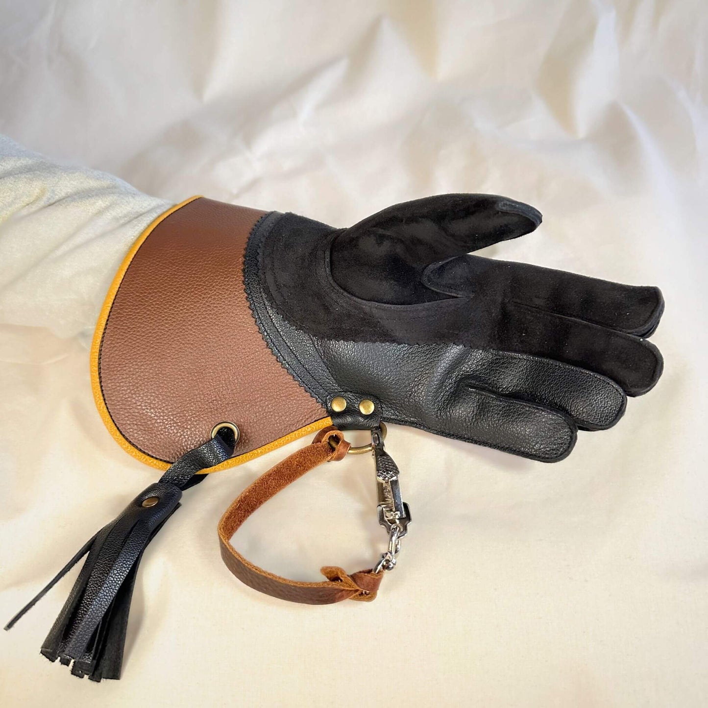 A short half-cuff falcon gauntlet made with brown and black suede deer leather looking at the palm with the (not included but available for purchase) French snap and leather thong.