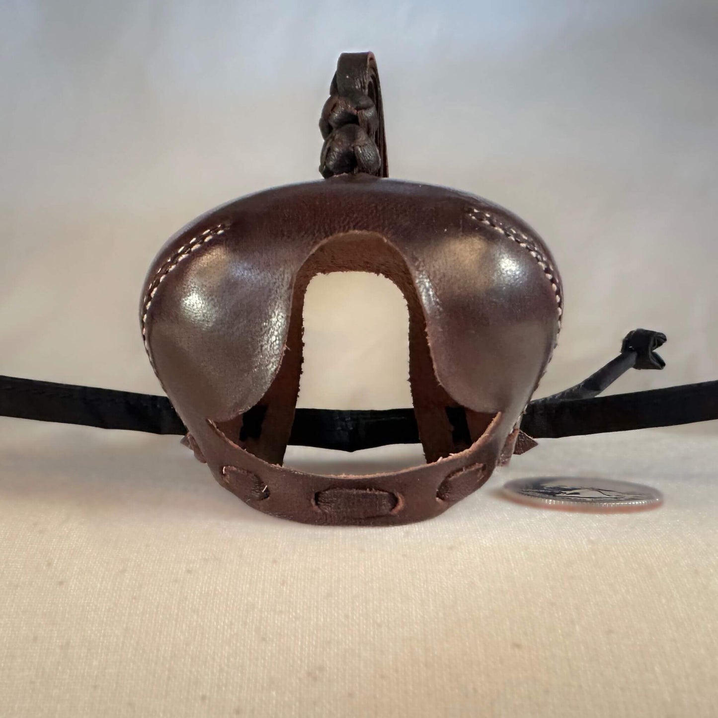 Falcon hood made of brown calf leather with a double knot top ornament facing forwards.