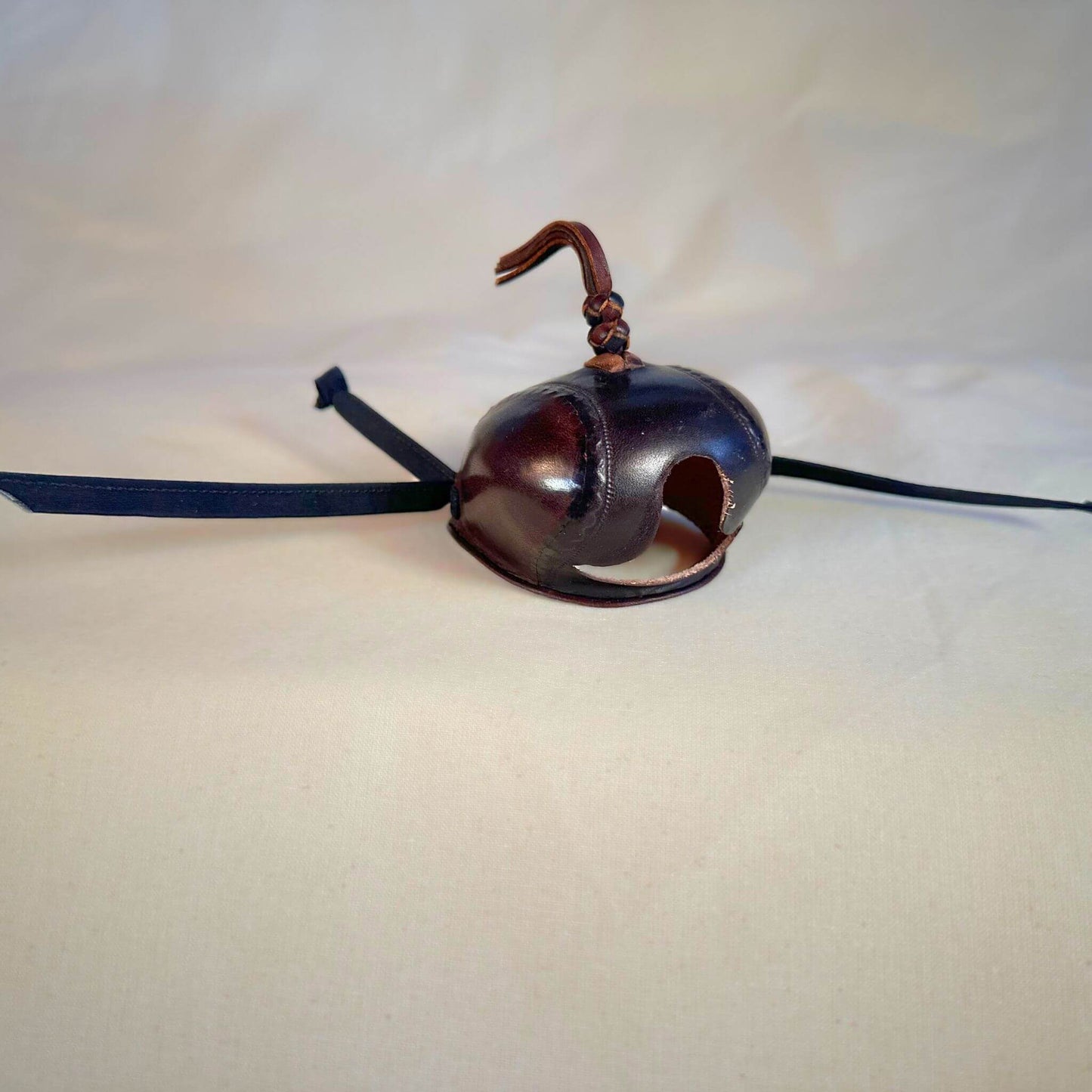 Falcon hood made of two-tone brown calf leather with a double knot top ornament at a three-quarter view.