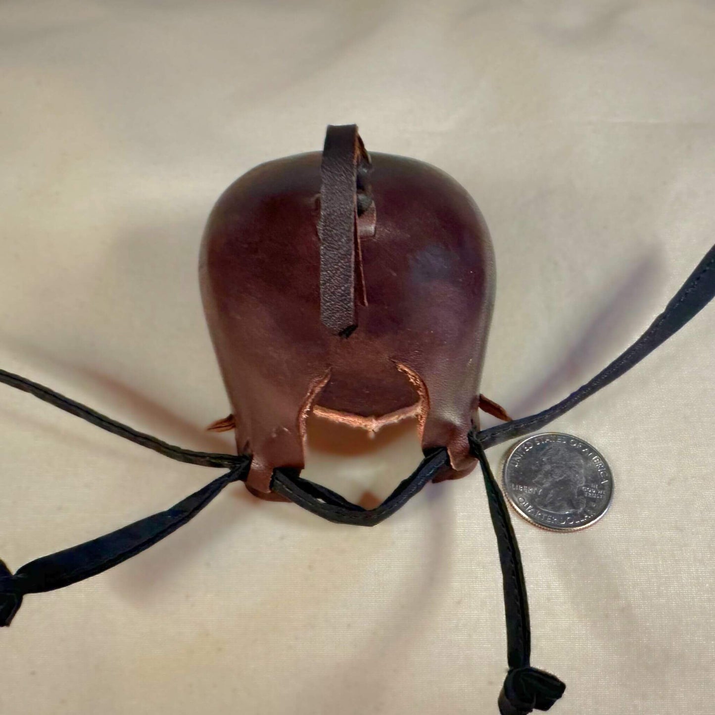 Falcon hood made of brown calf leather with a double knot top ornament in a back side view.