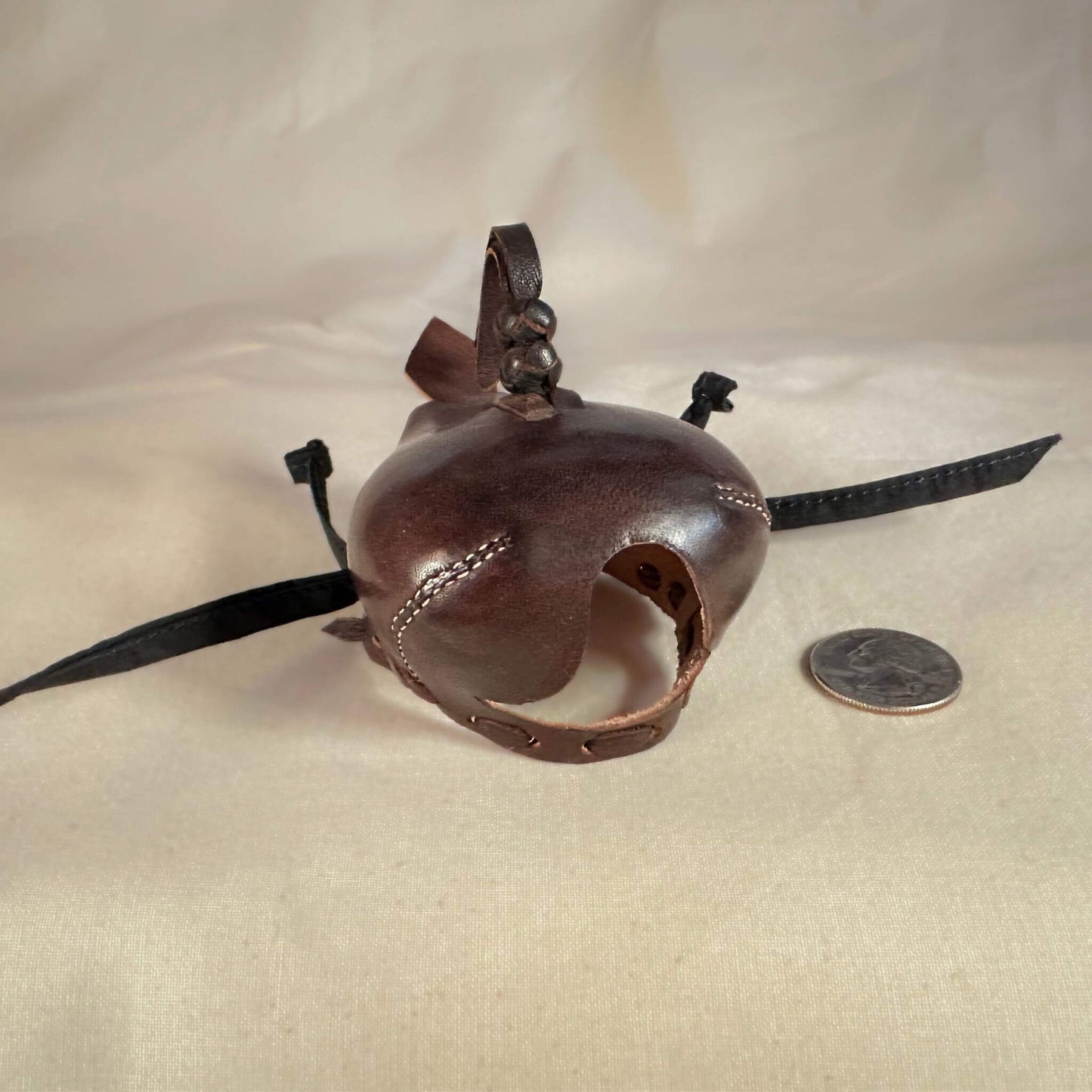 Falcon hood made of brown calf leather with a double knot top ornament looking down at a three-quarter view.