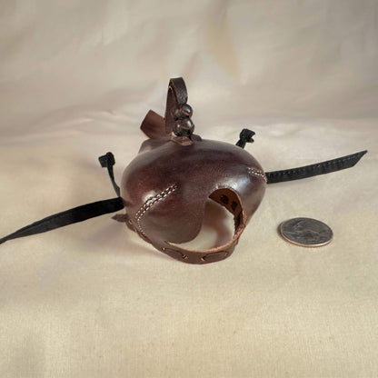 Falcon hood made of brown calf leather with a double knot top ornament looking down at a three-quarter view.
