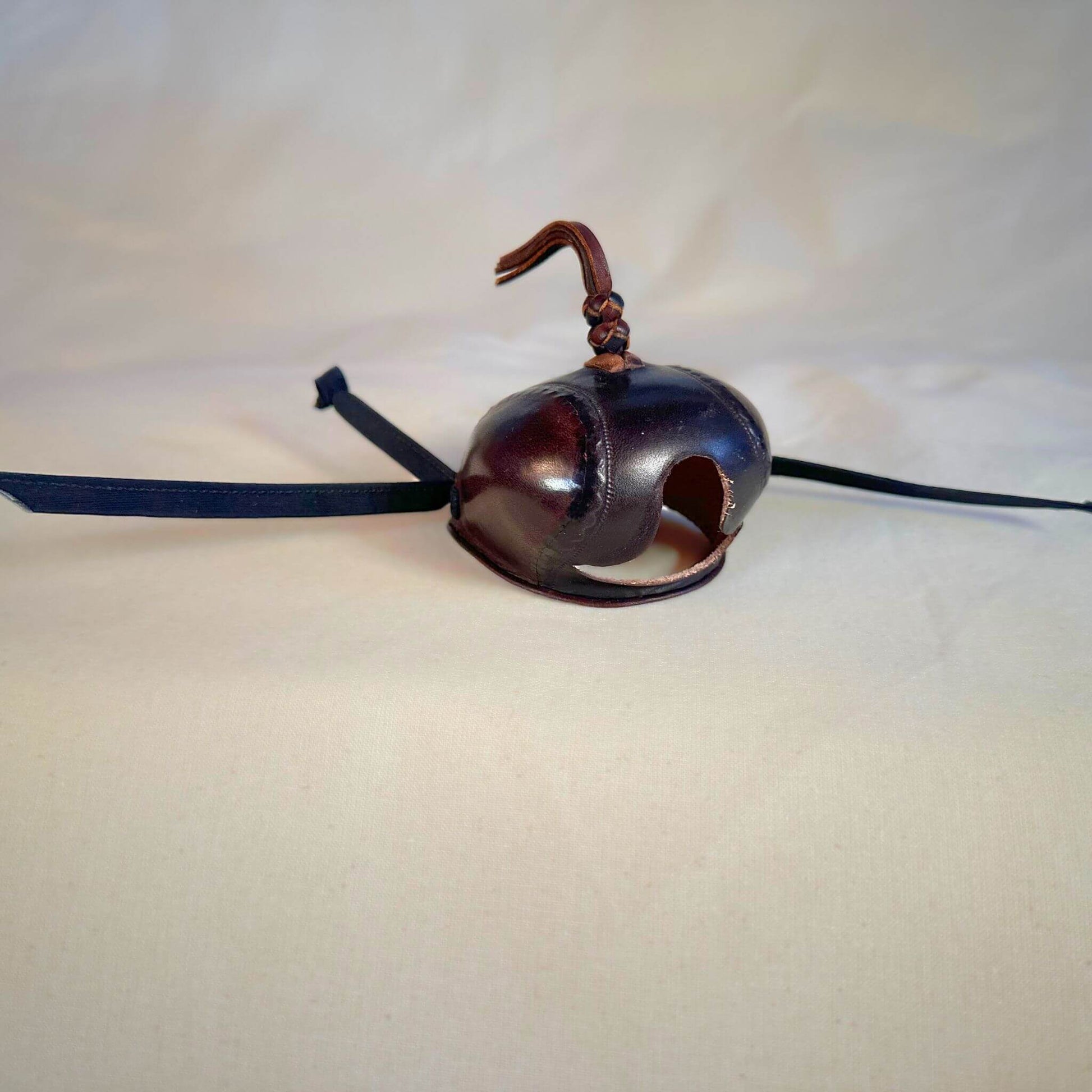 Falcon hood made of two-tone brown calf leather with a double knot top ornament at a three-quarter view.