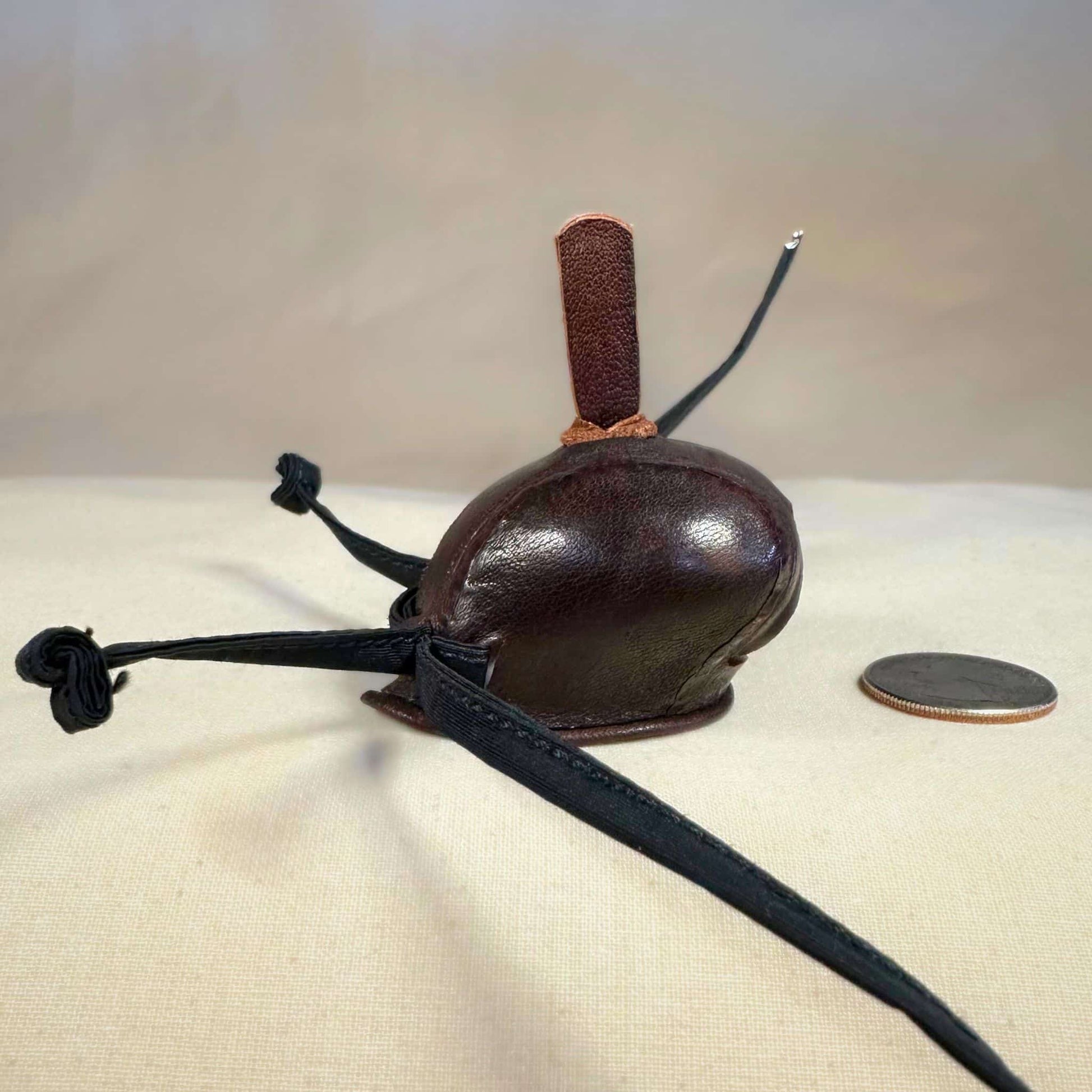 Mini falcon hood made of brown kangaroo leather with a top ornament looking from the right side.