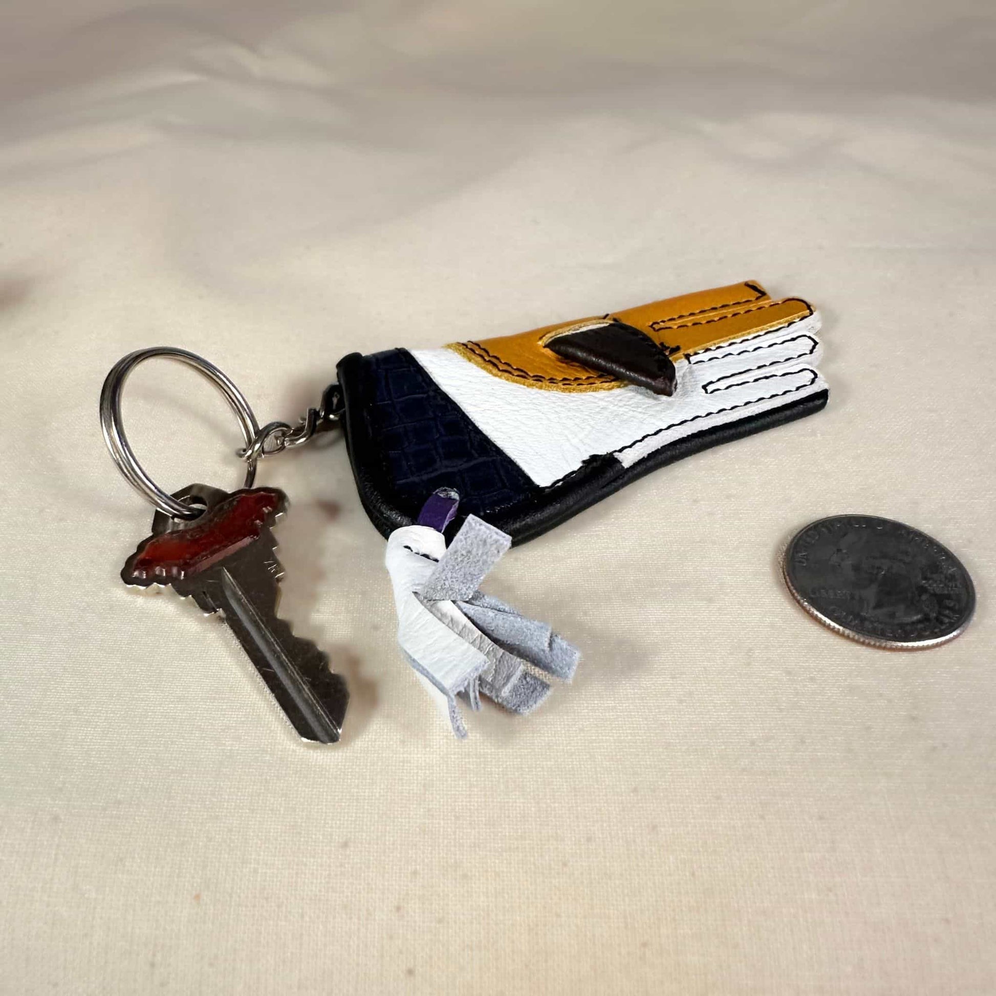 Miniature sewn gauntlet with a key ring laying flat.