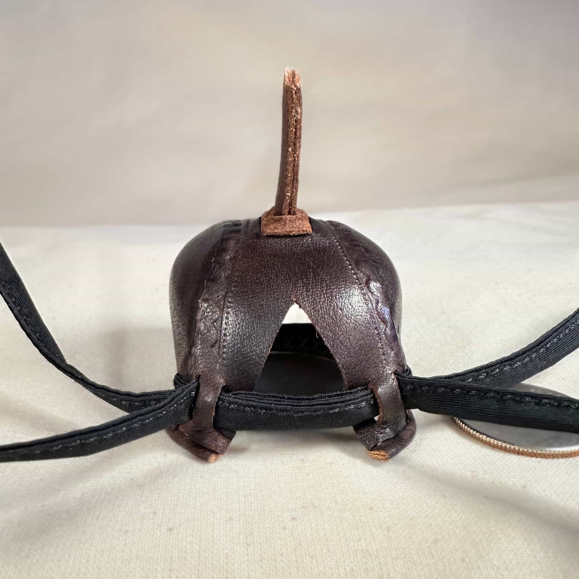 Mini falcon hood made of brown kangaroo leather with a top ornament looking at the back.