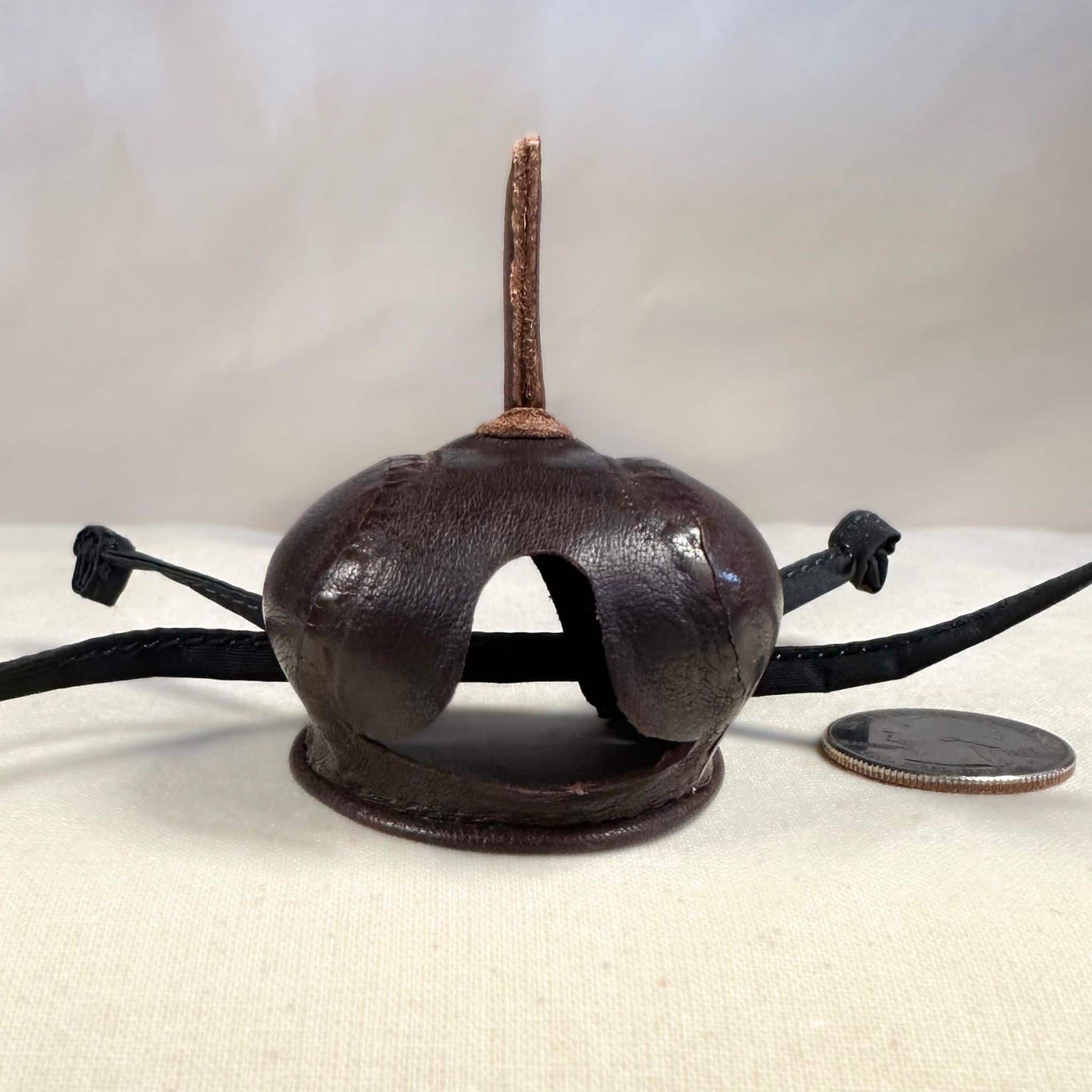 Mini falcon hood made of brown kangaroo leather with a top ornament looking at the front.